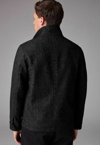 Jachetă neagră din lână amestecată cu un pattern herringbone, guler înalt și croială ajustată. Prezintă un spate curat cu manșete cu buton.