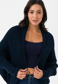 Tumesinine kootud kardigan ribidega tekstuuriga, avatud ees ja pikad varrukad. Kombineeritud tumeda ribidega lühikese toppiga ja teksapükste ning.