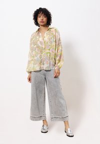 Blouse florale fluide de couleur pastel avec des manches longues ; associée à un jean gris pâle à jambe large et des mocassins argentés. Look simple et décontracté.