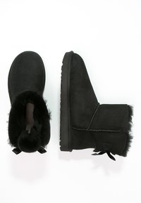 Bottines noires en daim doux, avec une doublure en fourrure confortable, dotées d'une semelle en caoutchouc texturée et d'un détail en nœud décoratif à l'arrière.