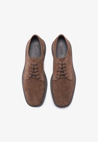 Scarpe in suede marrone con punta rotonda, sei occhielli e lacci neri. Presentano una suola texturizzata e cuciture a contrasto lungo i bordi.