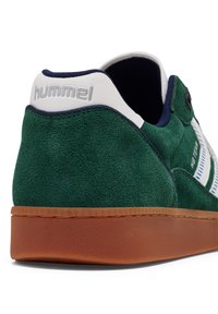 Grønne suede sneakers med hvide detaljer, tekstureret gummisåle og fremtrædende branding. Har en polstret krave og syede detaljer.