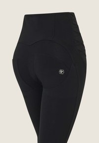Schwarze hochtaillierte Leggings mit glatter Textur, dekorativer Naht, kurvigen Nähten und einem kleinen Logo auf der Tasche.
