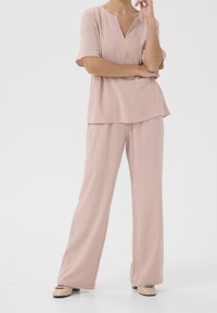 Top rosa chiaro, morbidamente aderente, con scollatura a V e maniche corte, abbinato a pantaloni a gamba larga dello stesso colore. Texture liscia, design casual.
