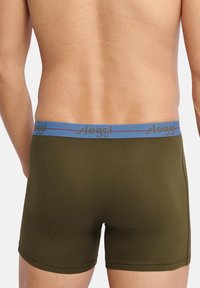 Boxer in verde oliva con elastico blu che presenta il nome del marchio "Sloggi" in un colore a contrasto. Design aderente e liscio.