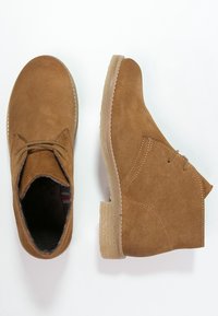 Bruine suède enkellaarsjes met een ronde neus, vetersluiting aan de voorkant en een getextureerde beige rubberen zool, met zichtbare stiksels en een zachte binnenvoering.