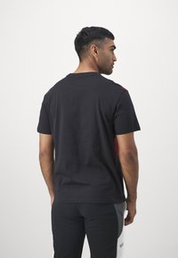 Juodas medvilninis T-shirt su trumpomis rankovėmis, su raudonu akcentu dešinėje pusėje. Minkšta tekstūra, apvalus iškirpimas ir įprastas kirpimas.