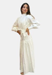 Vestito maxi in lino bianco con corpetto aderente, chiusura a bottoni e maniche a sbuffo; include una cintura da annodare in vita e una gonna a strati.