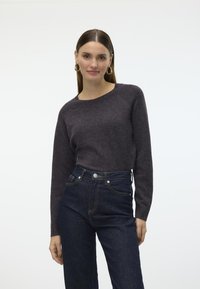 Maglione di lana grigio scuro con maniche lunghe e scollatura tonda, abbinato a jeans blu a vita alta. Design semplice con dettagli minimi.