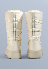 Beżowe ocieplane buty z puszystą nylonową cholewką, elastycznym ściągaczem na górze, bocznymi paskami i grubą gumową podeszwą.