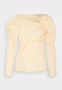 Krämfärgad långärmad blus med rynkade detaljer på puffärmarna och sned, samlad design över framsidan.