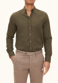 Olivengroene langemouwshirt met een button-down kraag, textuurstof en grijze knopen, gecombineerd met beige chino's.