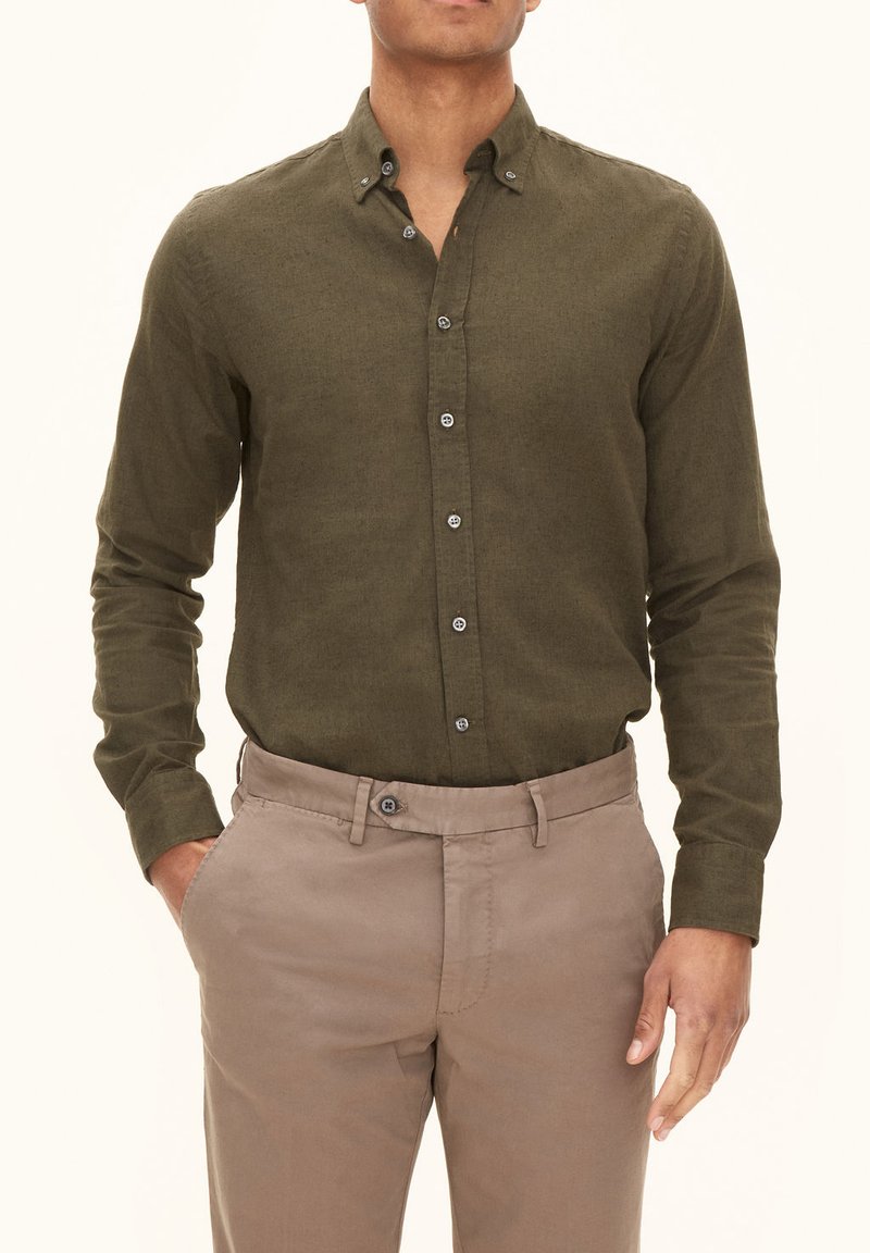 Olivengroene langemouwshirt met een button-down kraag, textuurstof en grijze knopen, gecombineerd met beige chino's.