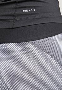 Camiseta atlética negra Dri-Fit combinada con leggings gris con patrón que presentan rayas diagonales y textura contrastante.