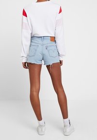 Vit sweatshirt med röda och rosa axelaccenter, matchad med ljusblå denimshorts med fransad nederkant och läderpatch med logotyp.