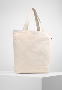 Torba na zakupy z płótna w kolorze off-white z dwoma górnymi uchwytami, w kształcie kwadratu, z przeszywanymi detalami i gładką fakturą. Brak widocznych elementów metalowych lub wzorów.