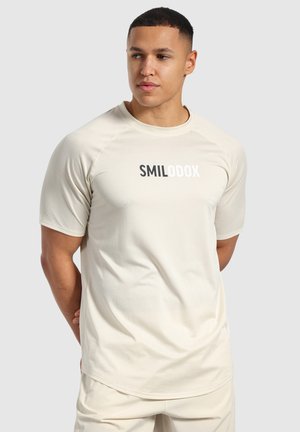Beige atletisk t-shirt med en åndbar mesh tekstur, korte ærmer, og "SMILODOX" logo i sort og hvid centreret på brystet.