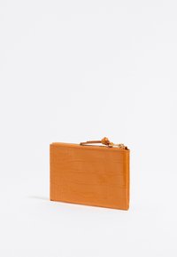 Orange crocodile-patterned wallet with a glossy finish, featuring a zip closure and a small leather pull tab. Slim rectangular shape.