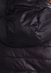 Chaqueta acolchada negra con una textura brillante y suave. Presenta una capucha y un patrón acolchado en el cuerpo para aislamiento y calor.