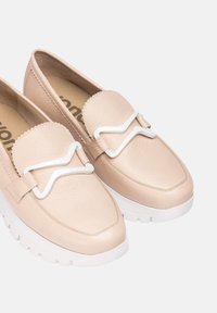 Mocasines de cuero beige con un acabado texturizado, que presentan un acento ondulado blanco en la correa y una suela gruesa blanca.