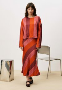 Haut à manches longues rayé rouge et rose associé à une jupe longue assortie. Tissu à texture lisse ; design de couleur en couches avec une silhouette fluide.