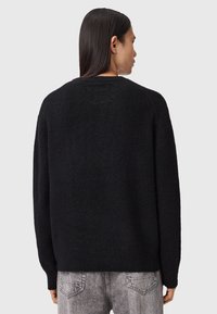 Man with long black hair wears a black fuzzy sweater and gray jeans, shown from the back against a plain light gray background.