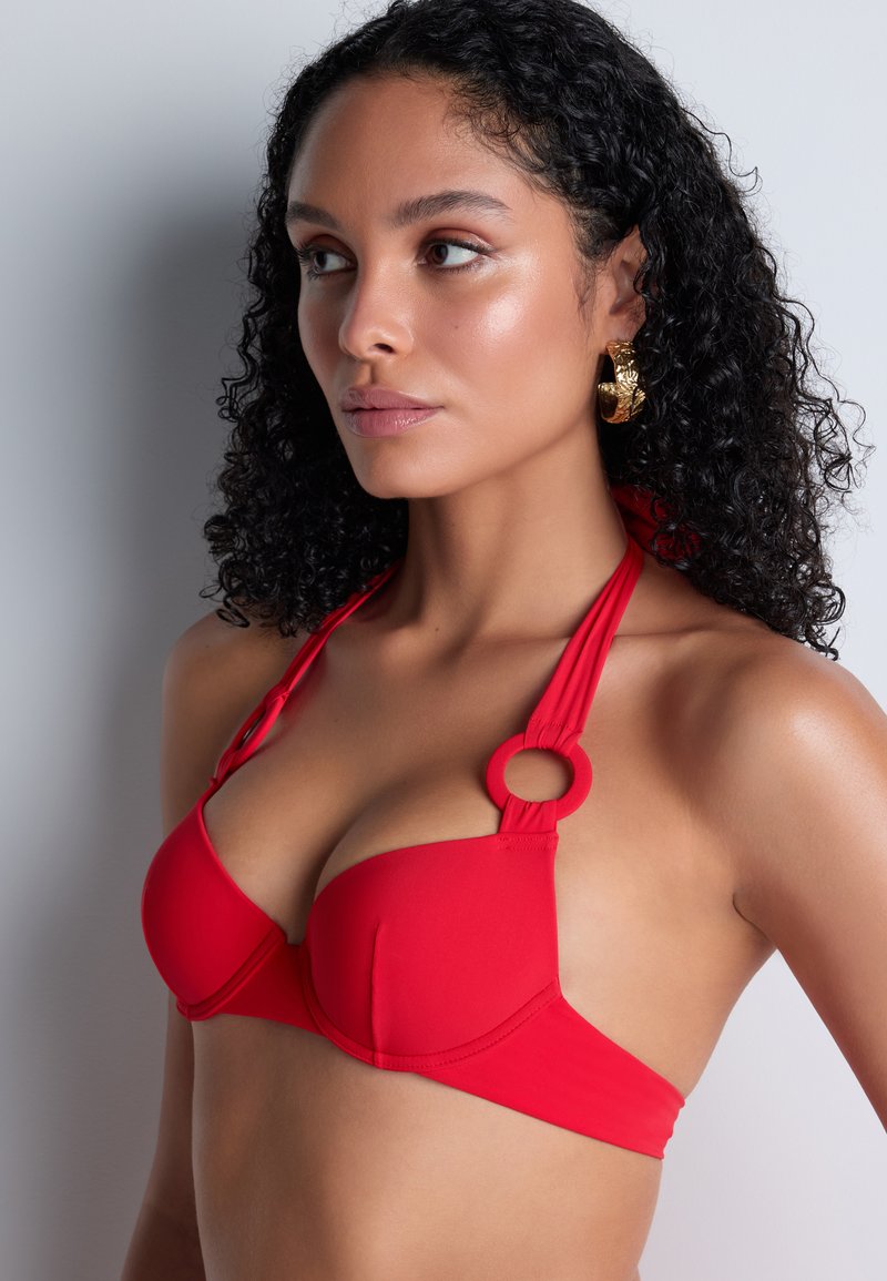 Haut de bikini rouge avec bonnets rembourrés, bretelles tour de cou avec un détail anneau, et texture de tissu lisse. Offre une coupe structurante.