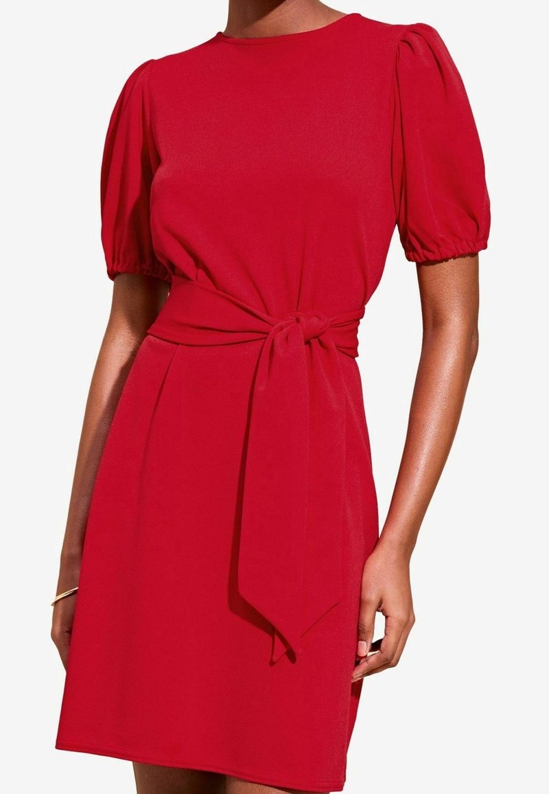 Robe rouge en tissu lisse, avec des manches bouffantes, un col rond et un détail noué à la taille pour une coupe ajustée.