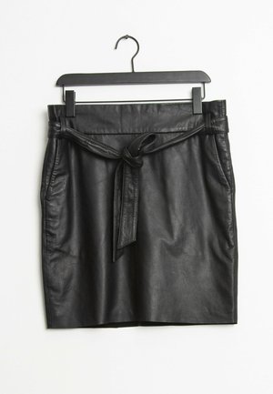 Jupe en cuir noire avec une ceinture nouée à la taille, suspendue sur un cintre noir sur fond blanc.