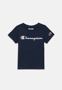 Mornarsko modra bombažna majica s kratkimi rokavi, ki ima bel "Champion" logo in majhno oznako na rokavu. Dva poklopna gumb na rami.
