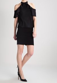 Top nero scollato con rouches, abbinato a una gonna nera aderente. Scarpe nere con tacco alto completano l'outfit. Tessuto morbido, design elegante.