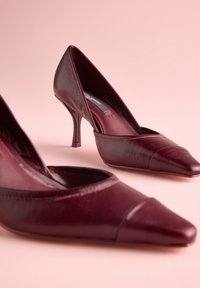 Bordové dámske lodičky na vysokom opätku so špicatou špičkou a textúrovaným koženým materiálom. Majú štíhly opätok a hladký, elegantný dizajn.