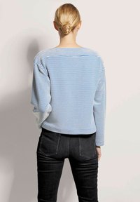 Gestreifter blau-weißer Pullover mit weiten Ärmeln, cropped Länge und rundem Ausschnitt, kombiniert mit schwarzen, eng anliegenden Jeans.