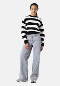 Pull rayé noir et blanc avec une texture côtelée, associé à un jean large gris clair et à des baskets grises.