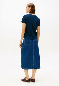 T-shirt a maniche corte blu navy abbinato a una lunga gonna di jeans. La gonna presenta tasche ed è abbinata a sneakers marroni.