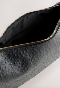 Black textured leather pouch with gold zipper partially open, showing smooth black fabric interior and a small inner zippered pocket.