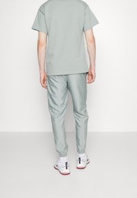 Ljusgrå t-shirt och matchande tapered träningsbyxor, tillverkade av mjukt material. Byxorna har elastiska manschetter; skorna har vita och röda detaljer.