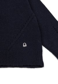 Tmavě modrý pletený svetr, který má ribbené manžety a okraje, s malým bílým logem v levém dolním rohu. Texturovaná tkanina s jemným prošíváním.