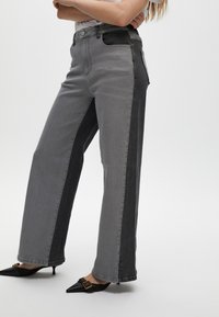 Grijze denim wide-leg jeans met contrasterende donkerdere zijpanelen, met een hoge taille, voorzakken en een rechte snit. Zwarte puntige schoenen.