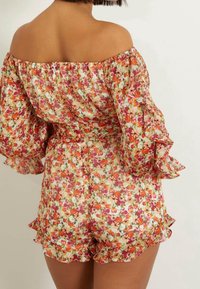 Romper floral décolleté aux manches évasées, mettant en avant un motif coloré de fleurs orange, rose et vert ; détail de bordure volante.