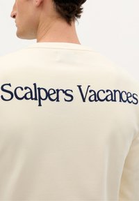Beige sweatshirt med "Scalpers Vacances" broderet i marineblå. Glat tekstur med rund halsudskæring og afslappet pasform.