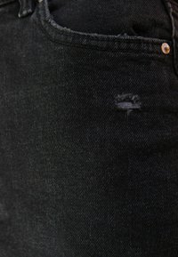 Jeans in denim nero con dettaglio consumato sull'area della tasca anteriore. Il tessuto è liscio con una texture sottile, caratterizzato da cuciture standard.