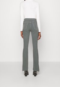 Grijze flared jeans met een hoge taille, een rafelige zoom en twee achterzakken. De stof lijkt gestructureerd en heeft een subtiele glans.