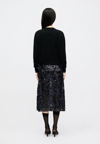 Sweater preto de mangas longas combinado com uma saia escura até ao joelho adornada com intricados e brilhantes lantejoulas pretas. Textura de tecido suave.