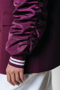 Burgundy jacket with a satin puff sleeve featuring gathered detailing, contrasted by a ribbed cuff with two white stripes.