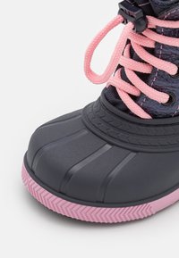 Schwarze wasserdichte Stiefel mit pinken Schnürsenkeln, Gummizehenschutz und strukturiertem Profil. Verfügt über ein glattes Obermaterial und einen pinken Akzent an der Sohle.