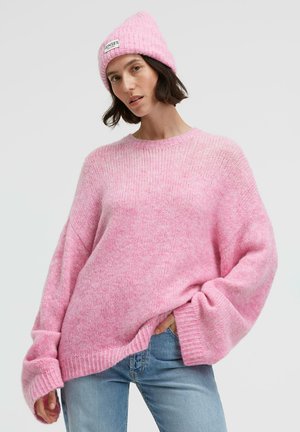 Pink oversized sweater made of soft knit fabric, featuring long sleeves and a ribbed hem. Paired with a matching pink beanie.
