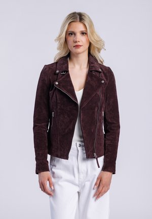 Veste de biker en daim bordeaux avec une fermeture éclair asymétrique, des revers crantés et des poches zippées. Associée à un pantalon blanc et un haut ajusté.