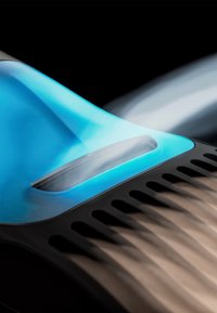 Tondeuse électrique bleue et noire coupant des cheveux bruns avec des lignes nettes visibles sur un fond noir.