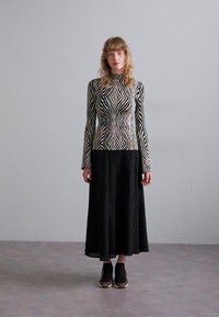 Maglietta a maniche lunghe a righe bianche e nere con collo alto, abbinata a una gonna plissettata nera e sneakers nere con dettagli leopardati.